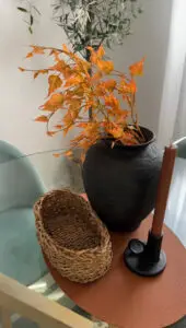 Photo d'un vase noir avec irrégularité posé au centre d'une table avec un bougeoir noir, une bougie marron et un panier en jonc de mer